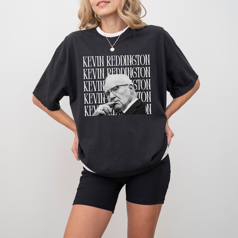 A woman wearing a black t-shirt with a graphic of a man's face and the text "KEVIN REDDINGTON" repeated across the shirt.