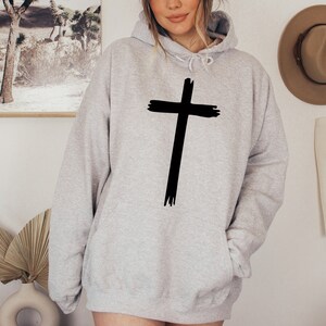 May include: A gray hooded sweatshirt with a black cross graphic on the front. The cross is stylized with a brushstroke effect.