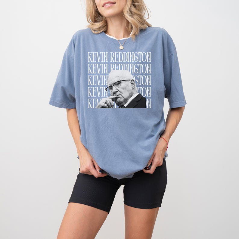 A woman wearing a blue t-shirt with a graphic of a man's face and the text "KEVIN REDDITION" printed on it.