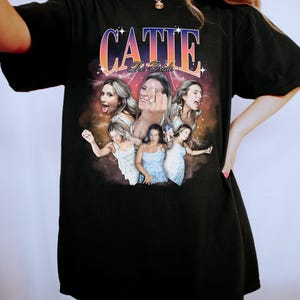 May include: Black oversized t-shirt with a graphic print of a group of women with the text "Catie The Bride" in a retro style.