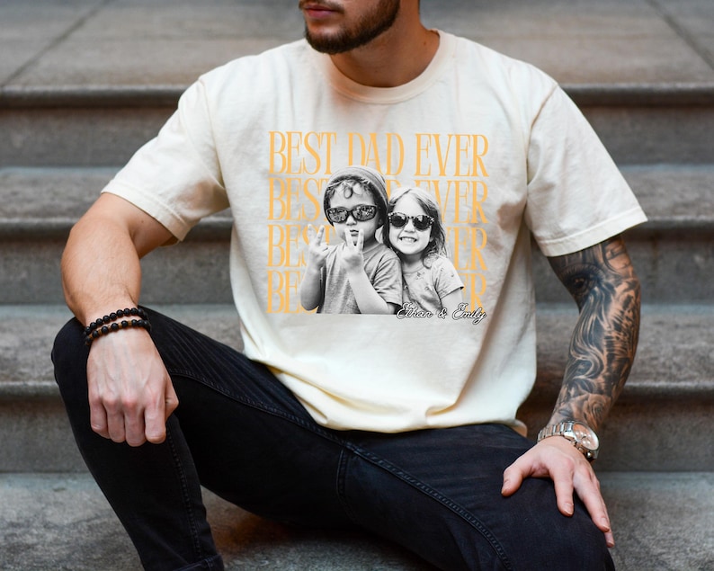 A man wearing a white t-shirt with a graphic design featuring two people, one of whom is wearing sunglasses.