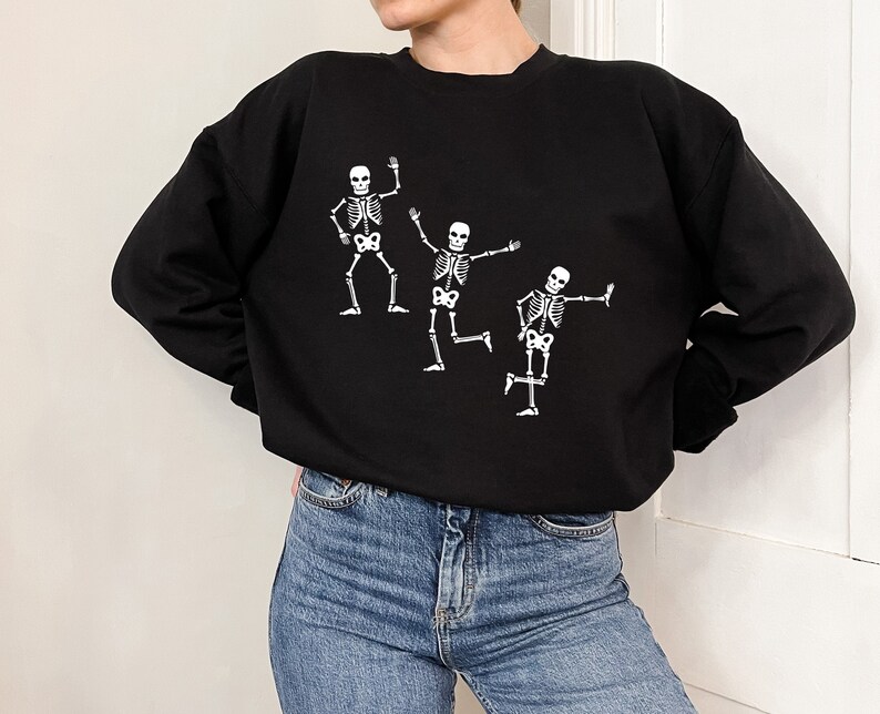 May include: Black sweatshirt with a white graphic of three skeletons dancing.