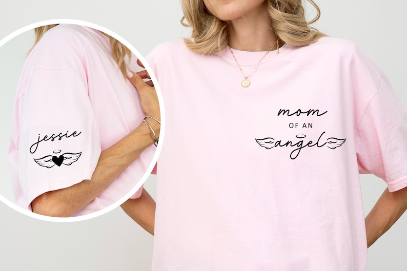 May include: A light pink t-shirt with the words "mom of an angel" in black script, along with a heart and wing design. The sleeve has the name "jessie" in script with a heart and wing design.