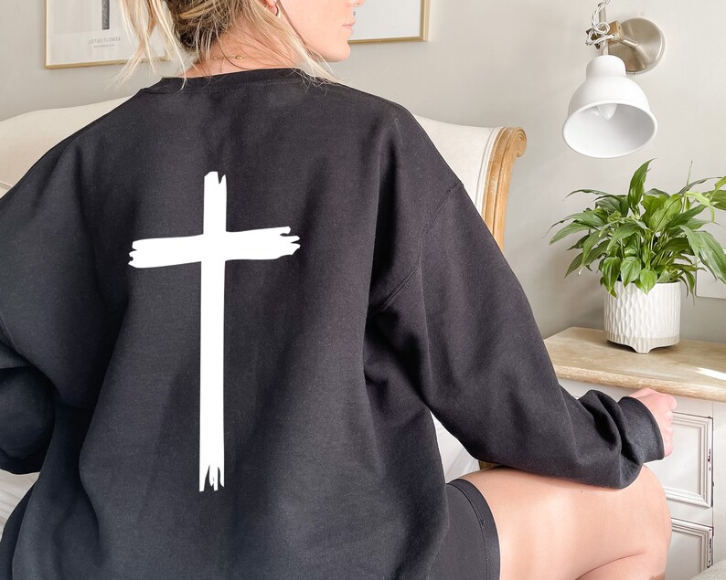 May include: Black sweatshirt with a white cross graphic on the back. The cross is drawn with a brushstroke effect.