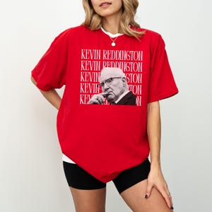 A woman wearing a red t-shirt with a graphic of a man's face and the text "KEVIN REDDINGTON" repeated across the shirt.