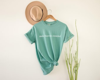 May include: A teal blue t-shirt with the text "make heaven crowded" printed in white on the front.