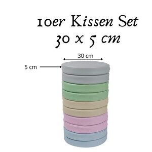 Könnte beinhalten: Ein Stapel aus 7 runden Kissen in verschiedenen Farben, darunter hellblau, hellgrün, beige und rosa. Jedes Kissen hat einen Durchmesser von 30 cm und ist 5 cm dick. Die Kissen sind in einem Stapel angeordnet, wobei das größte Kissen unten und das kleinste Kissen oben liegt. Der Text "Ioer Kissen Set 30 x 5 cm" ist über dem Kissenstapel sichtbar.