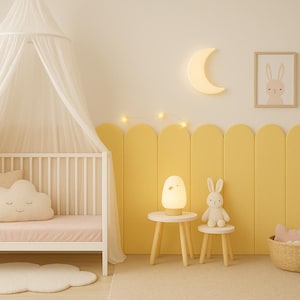 Pode incluir: Um quarto de crian&ccedil;a com um ber&ccedil;o branco, dossel e almofada em forma de nuvem. Uma parede de destaque amarela apresenta uma luz em forma de lua, arte emoldurada de coelhos e arco-&iacute;ris e uma pequena mesa com uma l&acirc;mpada e um brinquedo de coelho.