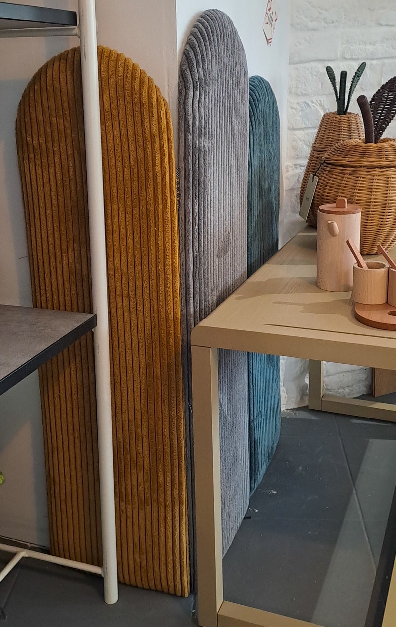 K&ouml;nnte beinhalten: Drei hohe, bogenf&ouml;rmige Wandpaneele, bezogen mit Kordstoff in Senfgelb, Hellgrau und Petrol. Die Paneele sind vertikal an einer Wand angebracht und weisen eine ausgepr&auml;gte gerippte Textur &uuml;ber ihre gesamte Oberfl&auml;che auf.