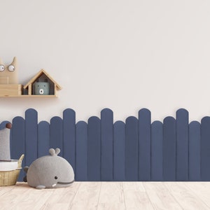 May include: A white wall with a wooden shelf holding two stuffed animal toys. Below the shelf is a blue fence with rounded tops. In the foreground, there is a wicker basket with a stuffed elephant toy and a gray whale stuffed animal.