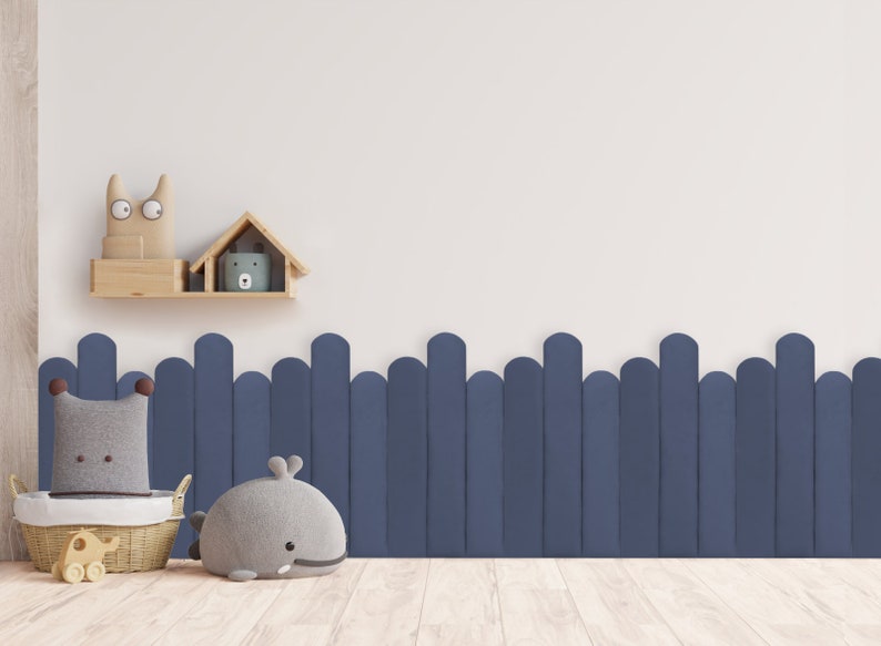 May include: A white wall with a wooden shelf holding two stuffed animal toys. Below the shelf is a blue fence with rounded tops. In the foreground, there is a wicker basket with a stuffed elephant toy and a gray whale stuffed animal.