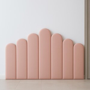 Pode incluir: Uma cabeceira rosa estofada com um design ondulado. A cabeceira &eacute; composta por sete ret&acirc;ngulos verticais e arredondados de alturas variadas. &Eacute; montada contra uma parede branca e repousa sobre um ch&atilde;o de cor clara.