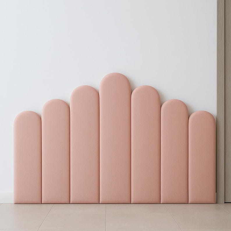 Pode incluir: Uma cabeceira rosa estofada com um design ondulado. A cabeceira &eacute; composta por sete ret&acirc;ngulos verticais e arredondados de alturas variadas. &Eacute; montada contra uma parede branca e repousa sobre um ch&atilde;o de cor clara.