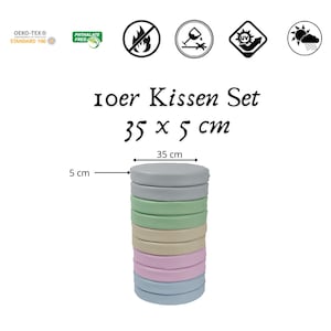Könnte beinhalten: Ein Set mit 10 runden Kissen in verschiedenen Pastellfarben, übereinander gestapelt. Die Kissen haben einen Durchmesser von 35 cm und sind 5 cm dick. Der Text "10er Kissen Set 35 x 5 cm" ist auf weißem Hintergrund gedruckt.