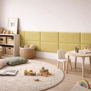 Op de afbeelding: Een kinderspeelkamer met een wand van rechthoekige limoengroene gestoffeerde panelen, een ronde tafel van licht hout met twee bijpassende stoelen, een groot rond beige tapijt, gevlochten opbergmanden en een witte kast met boeken.