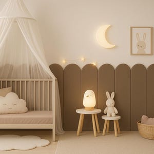 Pode incluir: Um quarto de crian&ccedil;a com uma cama branca, uma almofada em forma de nuvem e um dossel. Uma luz em forma de lua e arte emoldurada de um coelhinho e um arco-&iacute;ris adornam a parede. Uma pequena mesa sustenta uma l&acirc;mpada e um coelhinho de pel&uacute;cia.