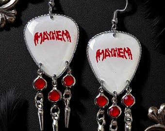 May include: A pair of silver-tone earrings with a white, guitar pick-shaped pendant. The word "MAYHEM" is printed in red on each pendant. Each earring features red gem accents and dangling silver spikes.
