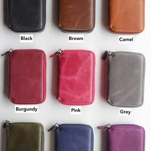 Puede incluir: Nueve carteras de cuero con cremallera de diferentes colores. Las carteras est&aacute;n dispuestas en tres filas de tres. Los colores son negro, marr&oacute;n, camel, burdeos, rosa, gris, verde marino, azul oscuro y morado.