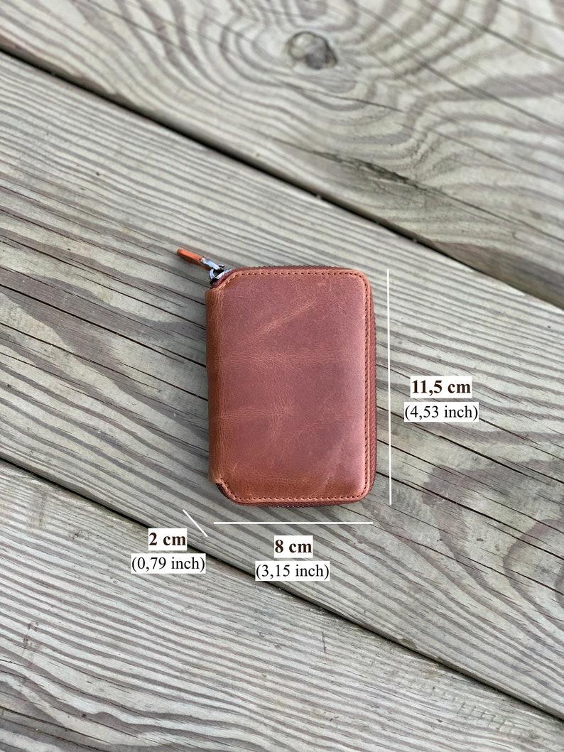 Puede incluir: Una cartera de cuero marr&oacute;n con cremallera y las siguientes medidas: 2 cm x 8 cm x 11,5 cm.