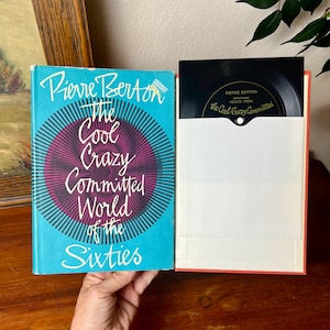Könnte beinhalten: Ein Vintage-Buch mit dem Titel "The Cool Crazy Committed World of the Sixties" von Pierre Berton, mit türkisblauem Einband und Retro-Design. Daneben eine Schallplattenhülle mit einer schwarzen Vinylplatte, die den gleichen Titel trägt.