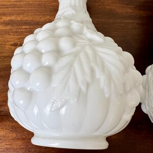 Puede incluir: Dos candelabros decorativos blancos. Cada soporte presenta un dise&ntilde;o detallado de racimo de uvas con hojas y una superficie texturizada. Los candelabros est&aacute;n hechos de un material blanco s&oacute;lido y tienen una apariencia cl&aacute;sica y elegante.