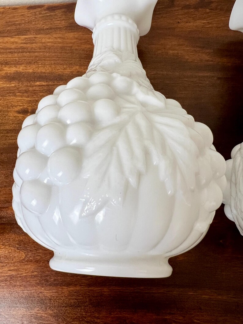 Puede incluir: Dos candelabros decorativos blancos. Cada soporte presenta un dise&ntilde;o detallado de racimo de uvas con hojas y una superficie texturizada. Los candelabros est&aacute;n hechos de un material blanco s&oacute;lido y tienen una apariencia cl&aacute;sica y elegante.