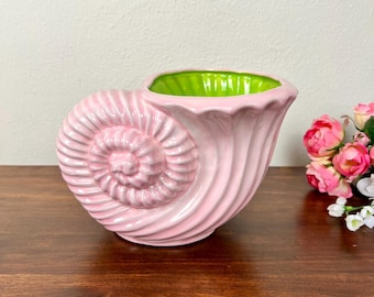 Puede incluir: Una maceta de cerámica con forma de concha de nautilo, con un exterior rosa claro brillante y un interior verde lima vibrante. La concha presenta un diseño en espiral con crestas elevadas y un borde festoneado, creando una apariencia texturizada.