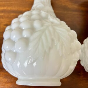 Puede incluir: Candelabros de vidrio blanco de estilo vintage. Los candelabros tienen un dise&ntilde;o de racimo de uvas en el cuerpo y un cuello acanalado. Los candelabros est&aacute;n hechos de vidrio blanco opaco.