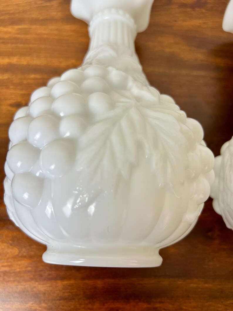 Puede incluir: Candelabros de vidrio blanco de estilo vintage. Los candelabros tienen un dise&ntilde;o de racimo de uvas en el cuerpo y un cuello acanalado. Los candelabros est&aacute;n hechos de vidrio blanco opaco.