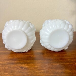 Puede incluir: Dos cuencos de vidrio blancos de estilo vintage con un dise&ntilde;o texturizado en forma de flor. Los cuencos son redondos con una base de pedestal y est&aacute;n sobre una superficie de madera. Los cuencos probablemente se utilizan para servir o exhibir.