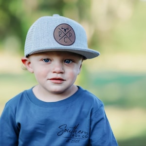 May include: A young person wearing a blue t-shirt with the text "Southern Boy Co. est 2020" and a gray and white baseball cap with a brown leather patch that says "RCP" with a deer head logo.