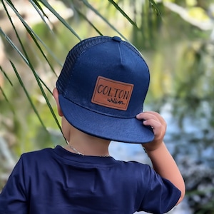 May include: A navy blue trucker hat with a brown leather patch that says "COLTON william".