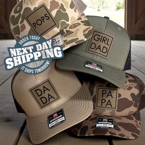 May include: Four trucker hats with mesh backs and square leather patches. The hats feature camouflage and solid tan or olive green colors. The patches are printed with the words POPS, GIRL DAD, DA DA, and PA PA. Each hat has a Richardson 112 label.