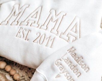 May include: White hooded sweatshirt with the text "MAMA EST. 2011" embroidered on the front and the names "Madison Landon Grayson" embroidered on the sleeve.