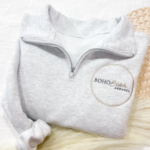 May include: A gray half-zip sweatshirt with a circular logo that says "BOHO Bloom APPAREL" in black text.