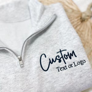 May include: A gray zippered sweatshirt with the text "Custom Text or Logo" in black.