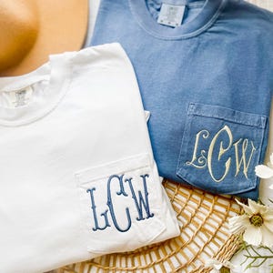 May include: A white short-sleeved t-shirt and a blue short-sleeved t-shirt, each featuring a chest pocket with the embroidered monogram LCW. The white shirt has dark blue embroidery, while the blue shirt has light cream-coloured embroidery.