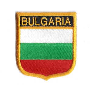 May include: Embroidered patch featuring the Bulgarian flag. The patch has a shield shape with a gold border. The flag design includes horizontal stripes of white, green, and red, with the word "BULGARIA" in gold letters on a black background.