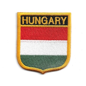 May include: Embroidered patch featuring the Hungarian flag. The patch has a shield shape with a gold border. The flag design includes horizontal stripes of red, white, and green, with the word "HUNGARY" in black letters at the top.