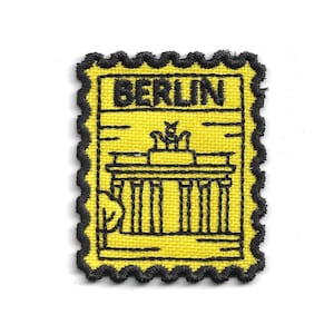 Può includere: Toppa gialla con bordi neri e la scritta "BERLIN" in alto. La toppa presenta un disegno a tratto nero di un edificio con colonne e un elemento decorativo in cima. La toppa ha la forma di un francobollo.