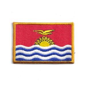 May include: Embroidered patch depicting the flag of Kiribati. The design shows a red background with a yellow sun and a bird above blue and white wavy lines, enclosed by a gold border. The patch is rectangular in shape.