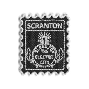 Puede incluir: Un parche bordado en blanco y negro con un borde festoneado. El parche presenta la palabra "SCRANTON" en la parte superior y la frase "THE ELECTRIC CITY" en un diseño circular. El diseño incluye un sol estilizado.