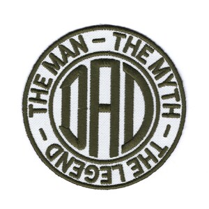 Könnte beinhalten: Ein weißer gestickter Aufnäher mit grünem Text, der "The Man - The Myth - The Legend" lautet, mit dem Wort "DAD" in einem Kreis in der Mitte.