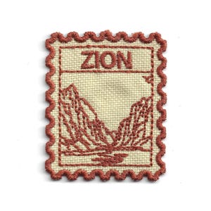 Puede incluir: Parche bordado con un diseño de paisaje montañoso y la palabra "ZION". El parche tiene un fondo crema con un borde y contorno de montaña rojos. El parche mide aproximadamente 5 cm por 5 cm.