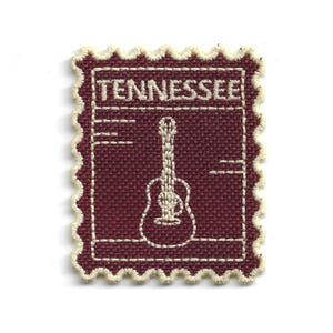 Puede incluir: Parche de tela granate con un diseño de guitarra bordada en blanco y la palabra "TENNESSEE". El parche tiene un borde dentado y un diseño de sello postal.