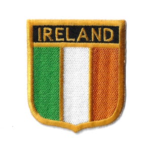 May include: An embroidered patch with the word "IRELAND" in yellow letters on a black background. The patch features the Irish flag with green, white, and orange stripes. The patch has a gold border and a shield shape.
