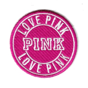 Könnte beinhalten: Rosa und weiß gestickter Aufnäher mit dem Text "LOVE PINK" in einem Kreis um das Wort "PINK".