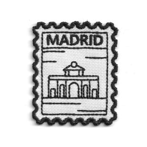 Peut inclure: Un écusson brodé rectangulaire avec un fond blanc et des coutures noires. Le motif présente un bord festonné, le mot MADRID en haut et une illustration au trait d'un bâtiment avec une entrée voûtée située au centre de l'écusson.
