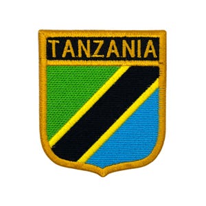 Può includere: Toppa ricamata con la scritta "TANZANIA" sopra un disegno a scudo. Lo scudo presenta sezioni verdi, nere, gialle e blu, con un bordo dorato. La toppa è destinata all'applicazione su abbigliamento o accessori.
