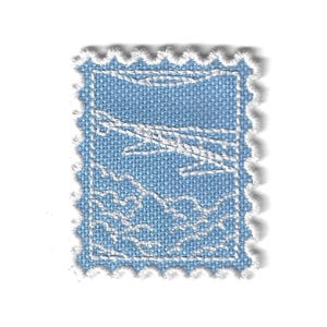 May include: A light blue embroidered patch shaped like a postage stamp with a white stitched border. The design features a white outline of an airplane flying above a landscape of clouds and mountains, all rendered in detailed thread work.